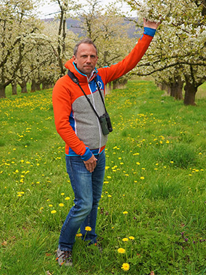 Umweltminister Thorsten Glauber steht auf einer Streuobstwiese zwischen weiß blühenden Obstbäumen