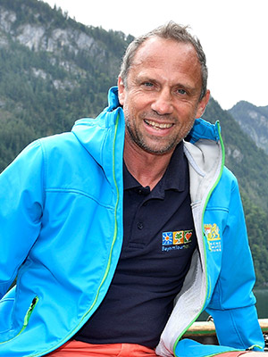 Umweltminister Thorsten Glauber lächelt vor einem Bergsee mit Bergpanorama sitzend in die Kamera