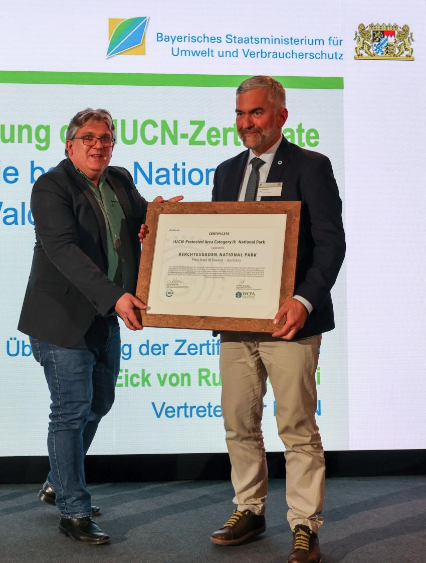 Dr. Eick von Ruschkowski und Dr. Roland Baier stehen auf der Bühne und halten zusammen das IUCN-Zertifikat.