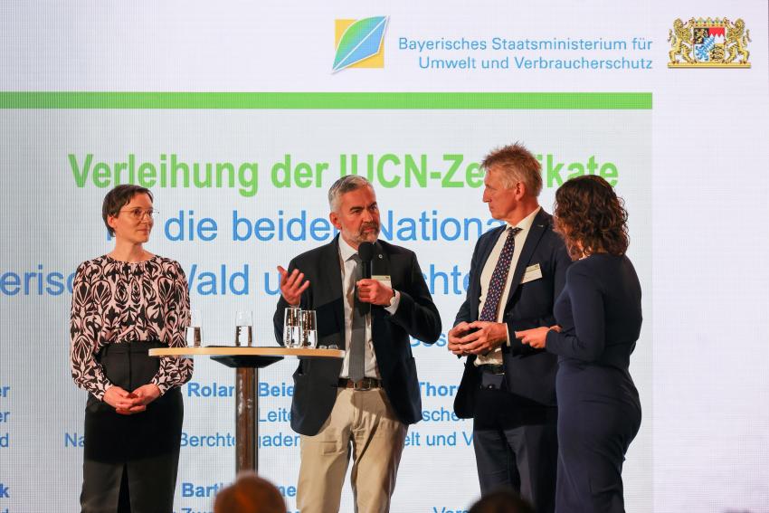 Auf der Bühne am Stehtisch stehen Leiterin des Nationalparks Bayerischer Wald Ursula Schuster (Foto links), Dr. Roland Baier (Leiter des Nationalparks Berchtesgaden) spricht ins Mikrofon und Peter Südbeck (Vorstandsvorsitzender bei Nationale Naturlandschaften e. V.).