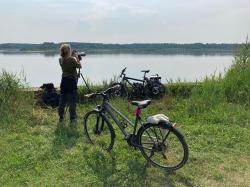 Eine Frau steht mit einem Spektiv am Wasser, neben ihr ein Fahrrad.